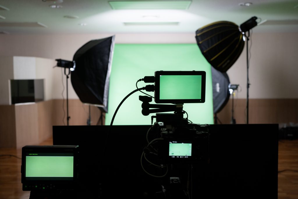 Selective focus of three screen attaching with camera while capturing a green screen cloth backdrop with a blurred green backdrop and an illuminated LED softbox lights in the background in the studio.